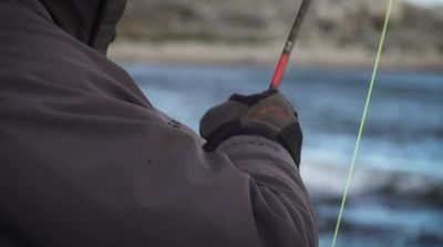 a man holding a fishing rod while standing next to a body of water