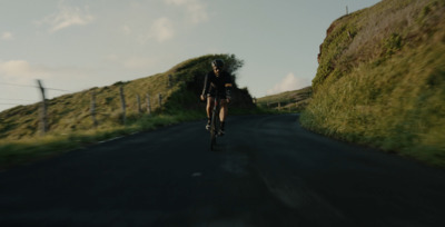 a man riding a bike down a road next to a lush green hillside