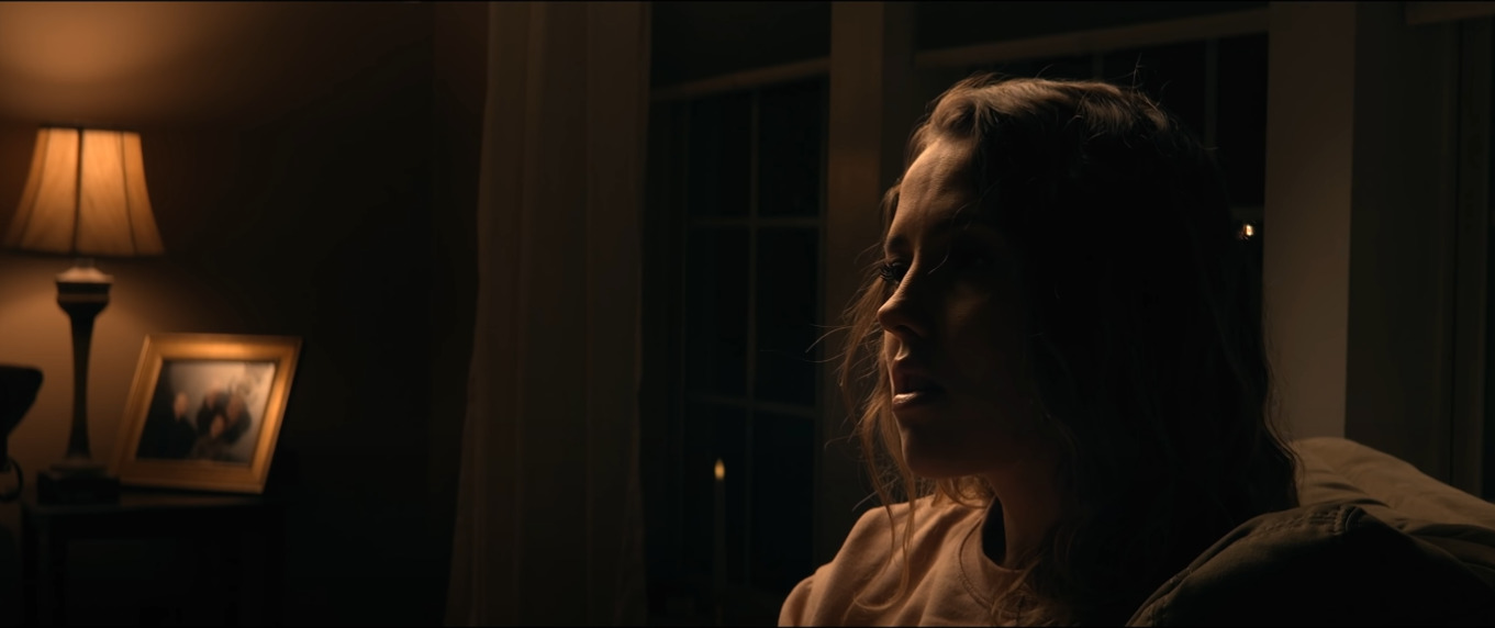 a woman standing in a dark room with a lamp on