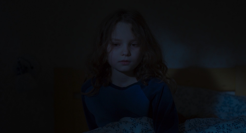 a young girl sitting on a bed in a dark room