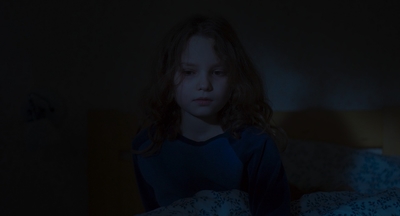 a young girl sitting on a bed in a dark room