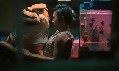 a man holding a stuffed animal next to a fish tank