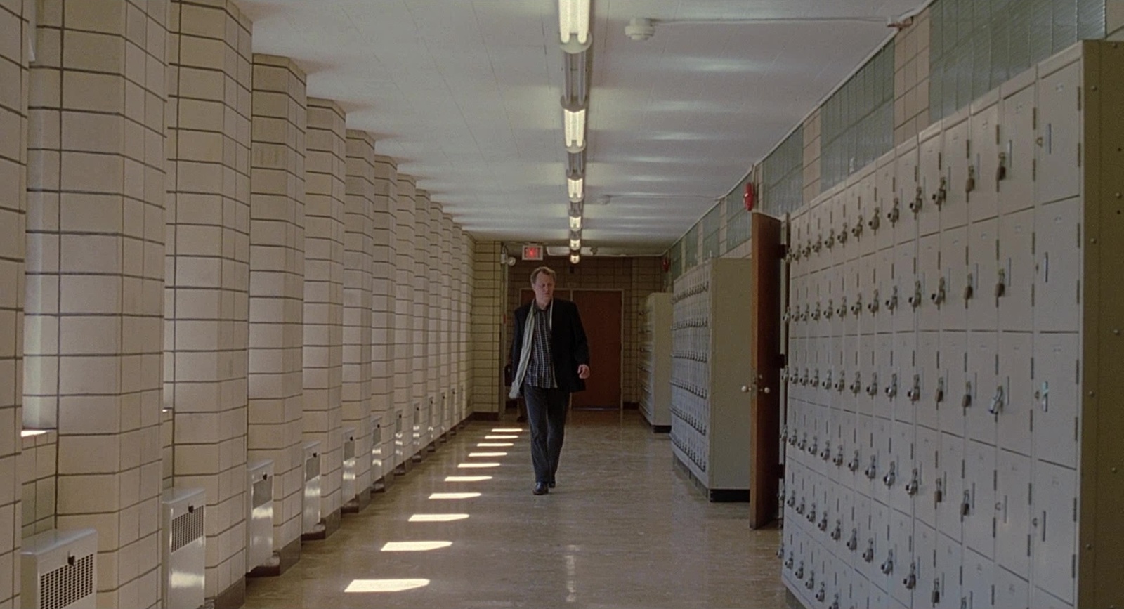 a man walking down a hallway between rows of lockers