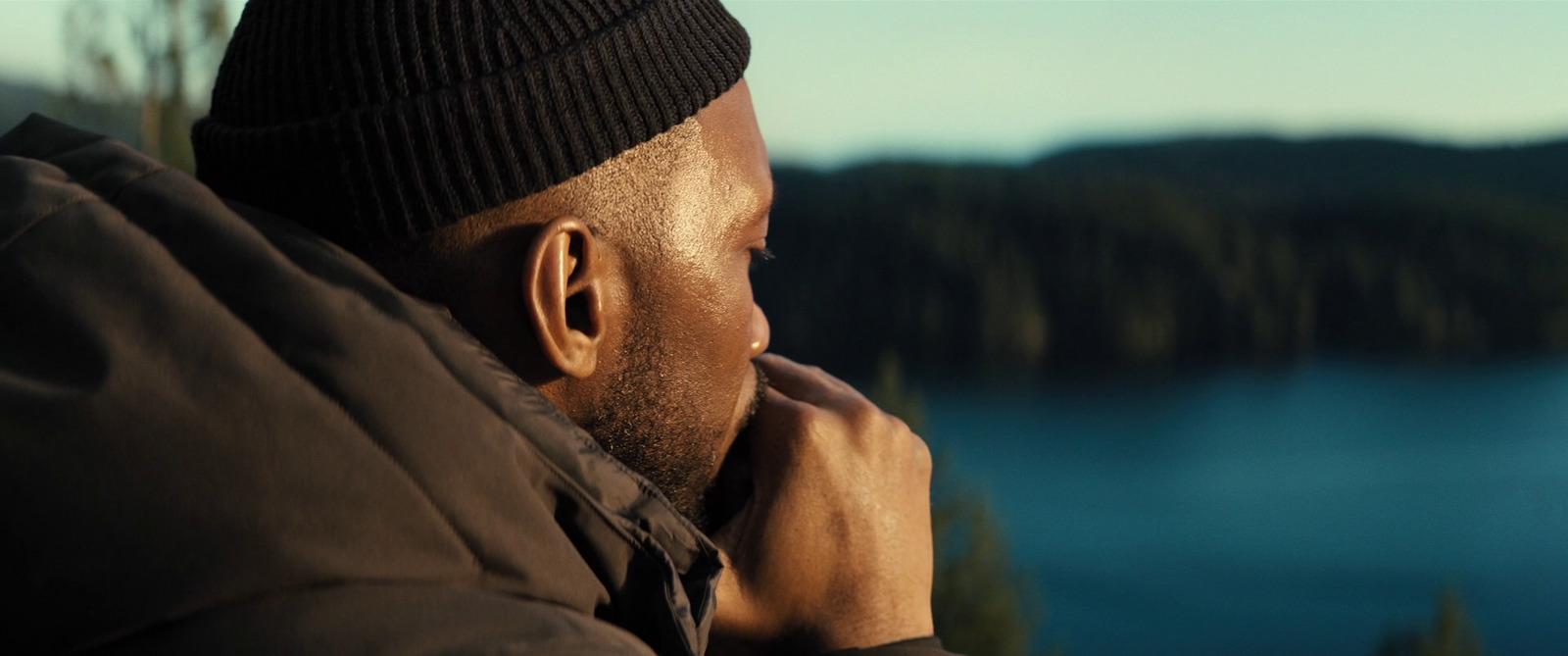 a man in a beanie looks out over a lake