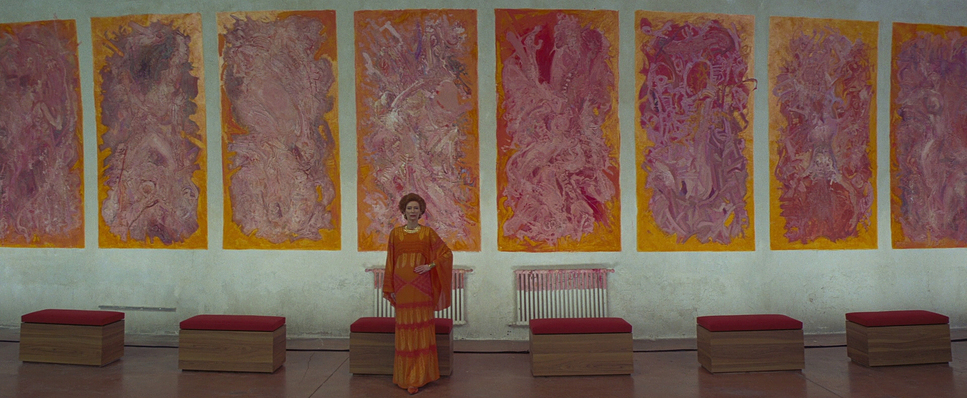 a woman standing in front of a wall with paintings on it