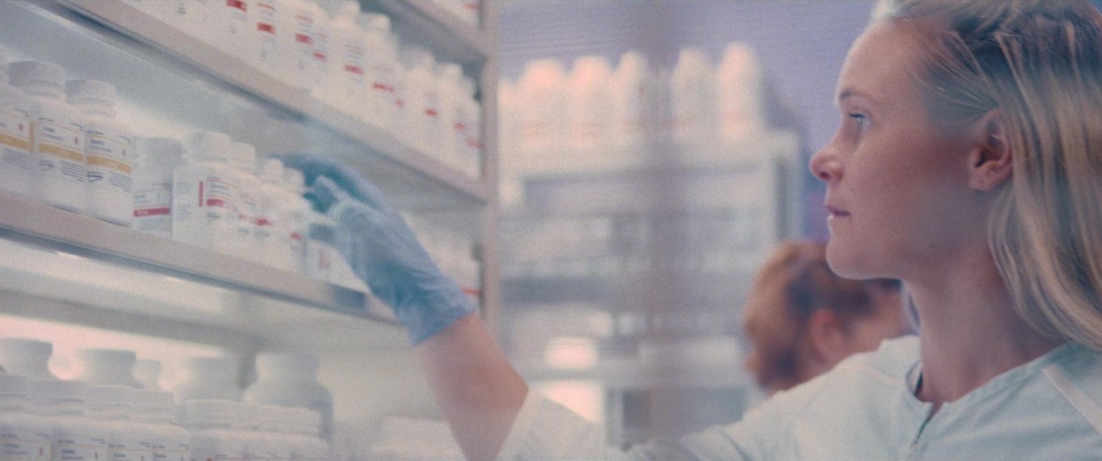 a woman in a white lab coat is looking at bottles