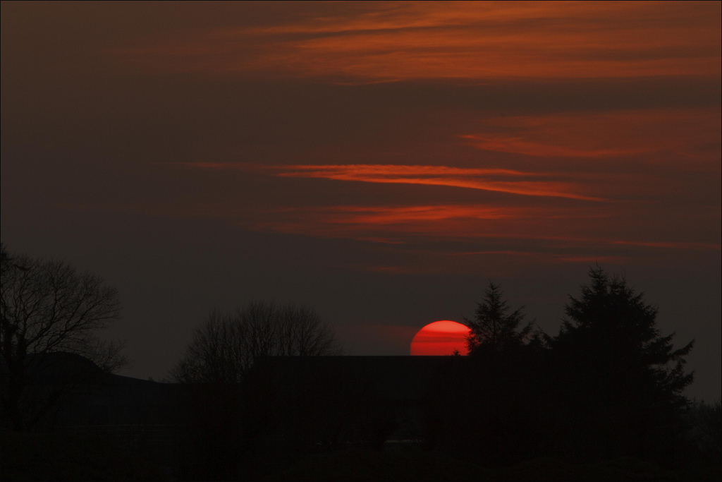 the sun is setting in the sky behind some trees