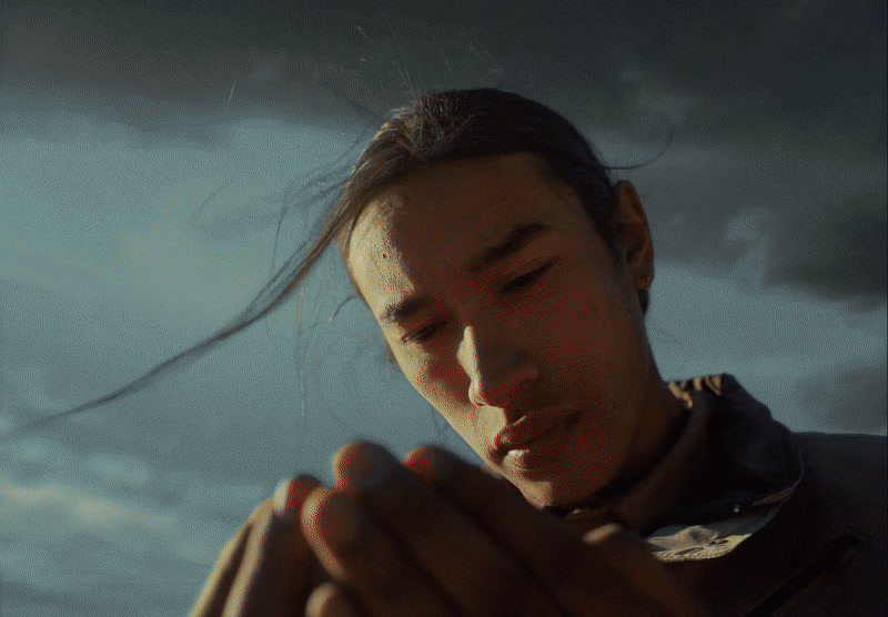 a man holding his hands together in front of a cloudy sky