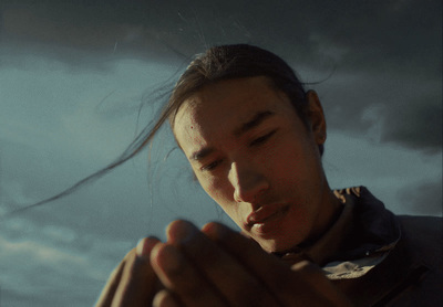 a man holding his hands together in front of a cloudy sky