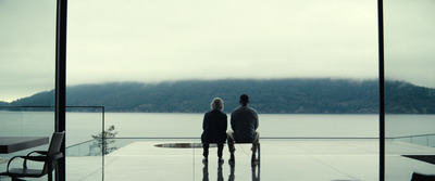 two people sitting on a bench looking out at a lake