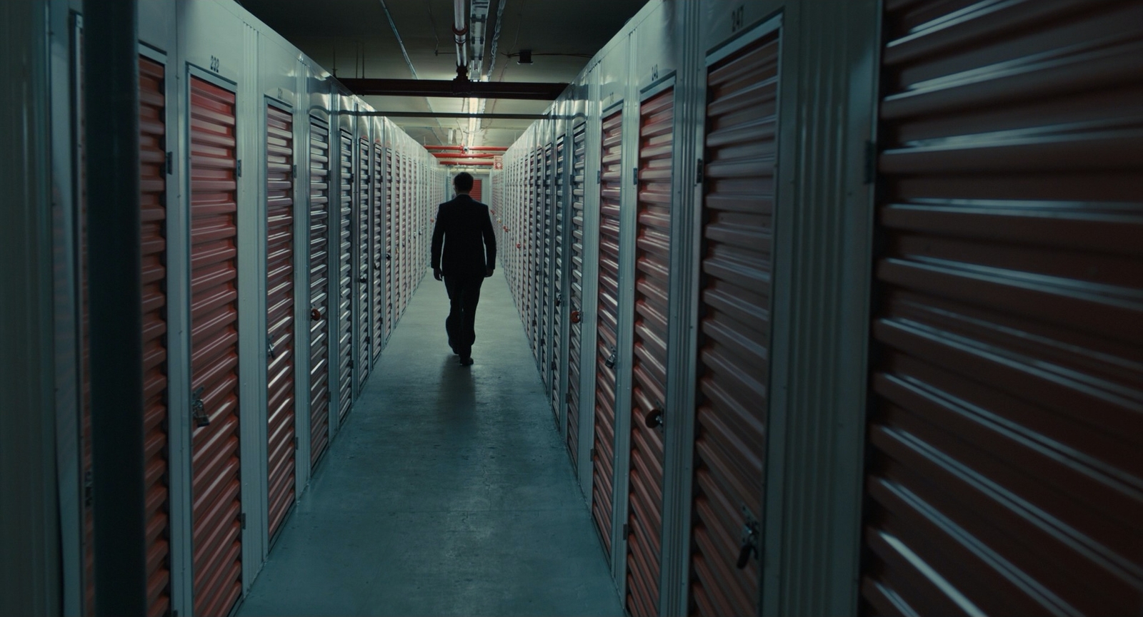 a man walking down a hallway between rows of storage units