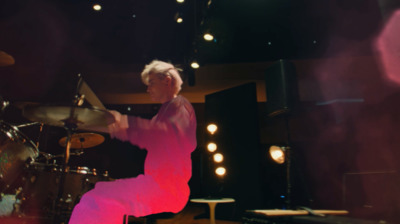 a man in a pink outfit is playing drums