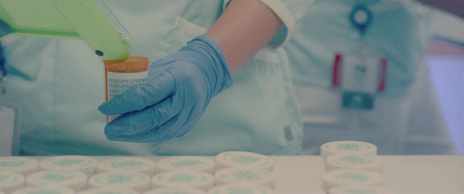 a person in blue gloves holding a bottle of medicine