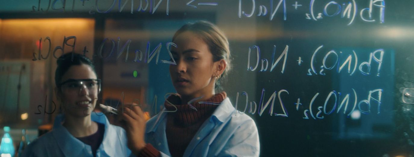 two women standing next to each other in front of a blackboard