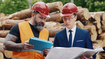 two men in hard hats are looking at a piece of paper