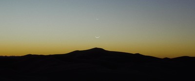 the moon is setting over a mountain range