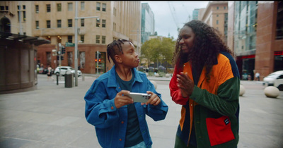 two people standing on a city street looking at a cell phone