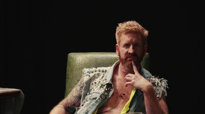 a shirtless man sitting in a chair with a glass of wine