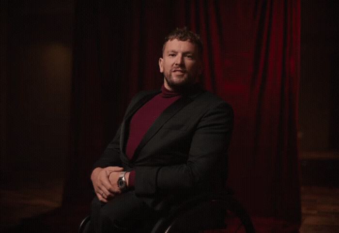 a man sitting in a chair in front of a red curtain