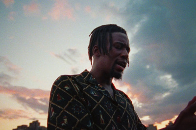 a man with dreadlocks standing in front of a sunset