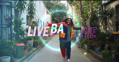 a woman walking down a sidewalk with a live ba sign in the background