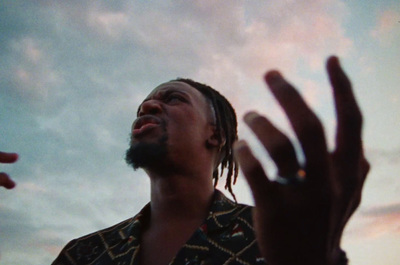 a man with dreadlocks standing in front of a cloudy sky