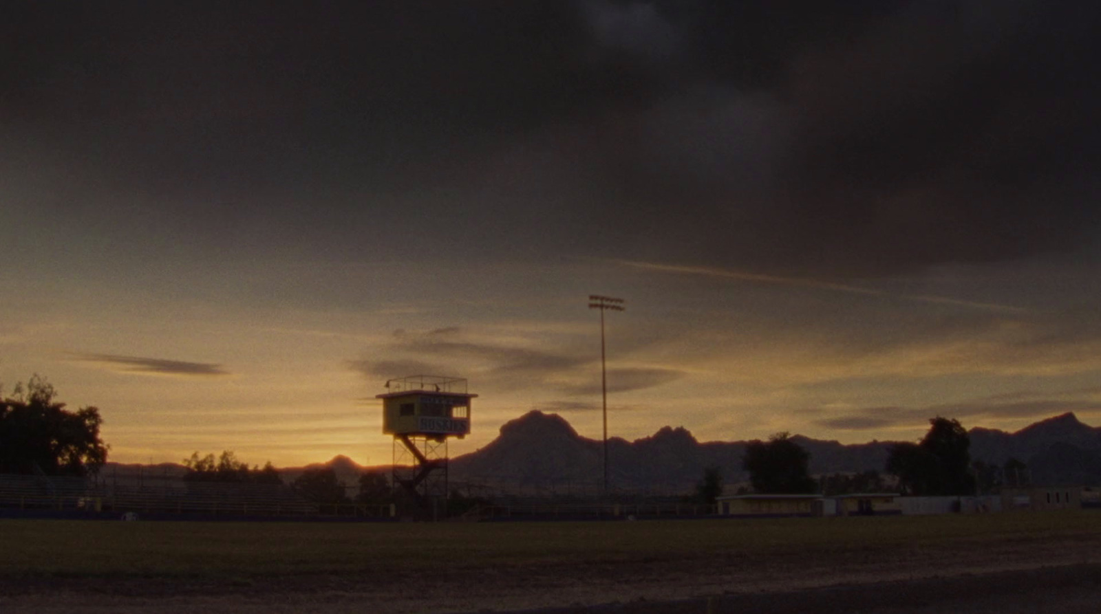 the sun is setting over a field with mountains in the background