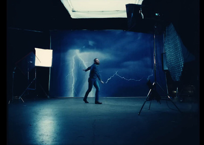 a man standing in a dark room with a lightning scene behind him