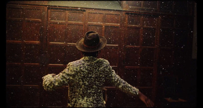 a man in a hat standing in front of a wooden door