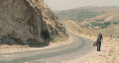 a woman standing on the side of a road holding a skateboard