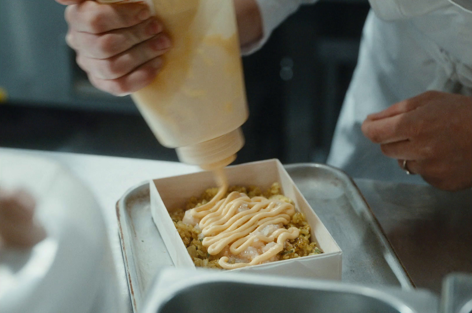 a person pouring sauce into a container of food