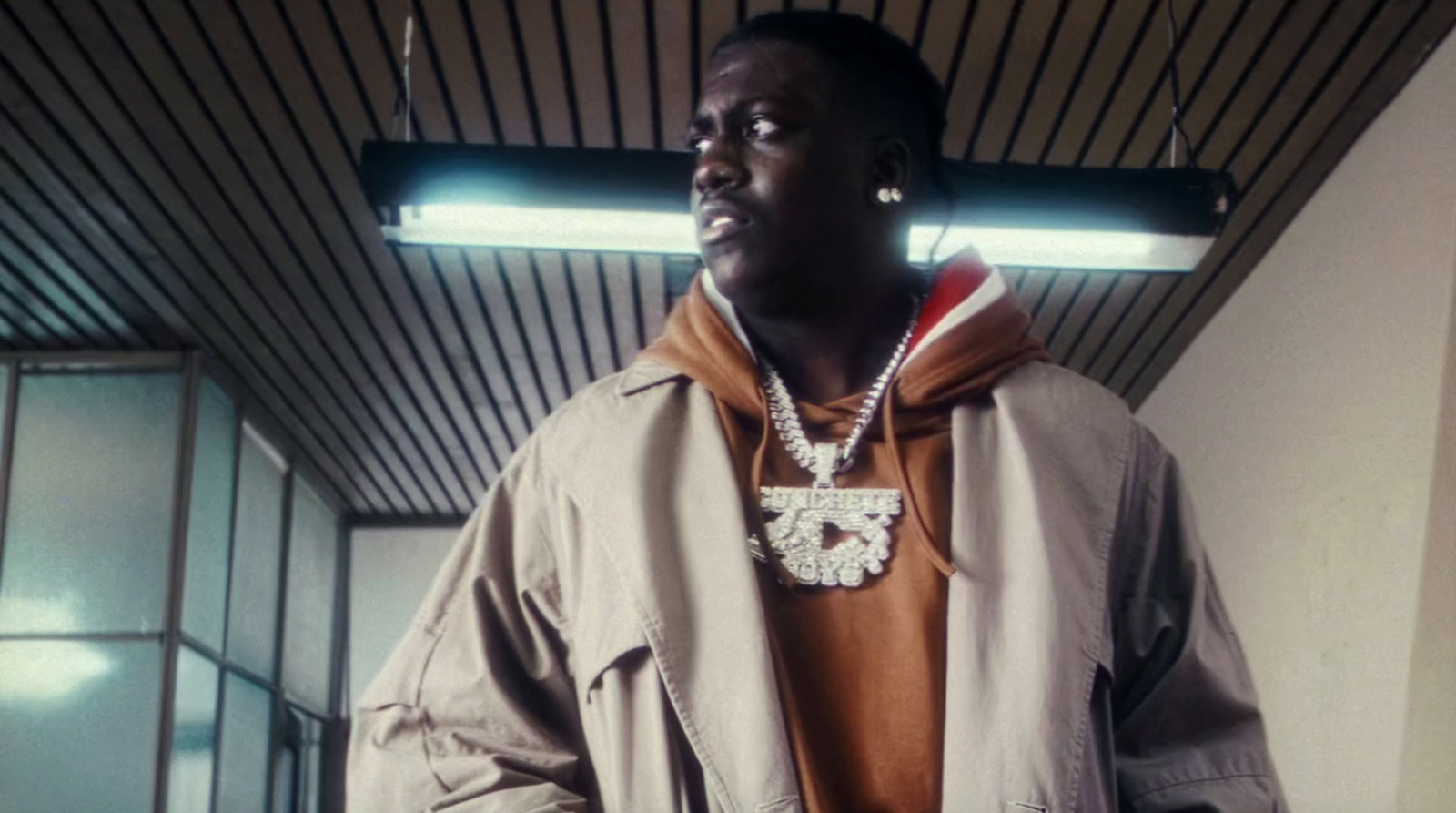 a man standing in a room wearing a jacket and a necklace