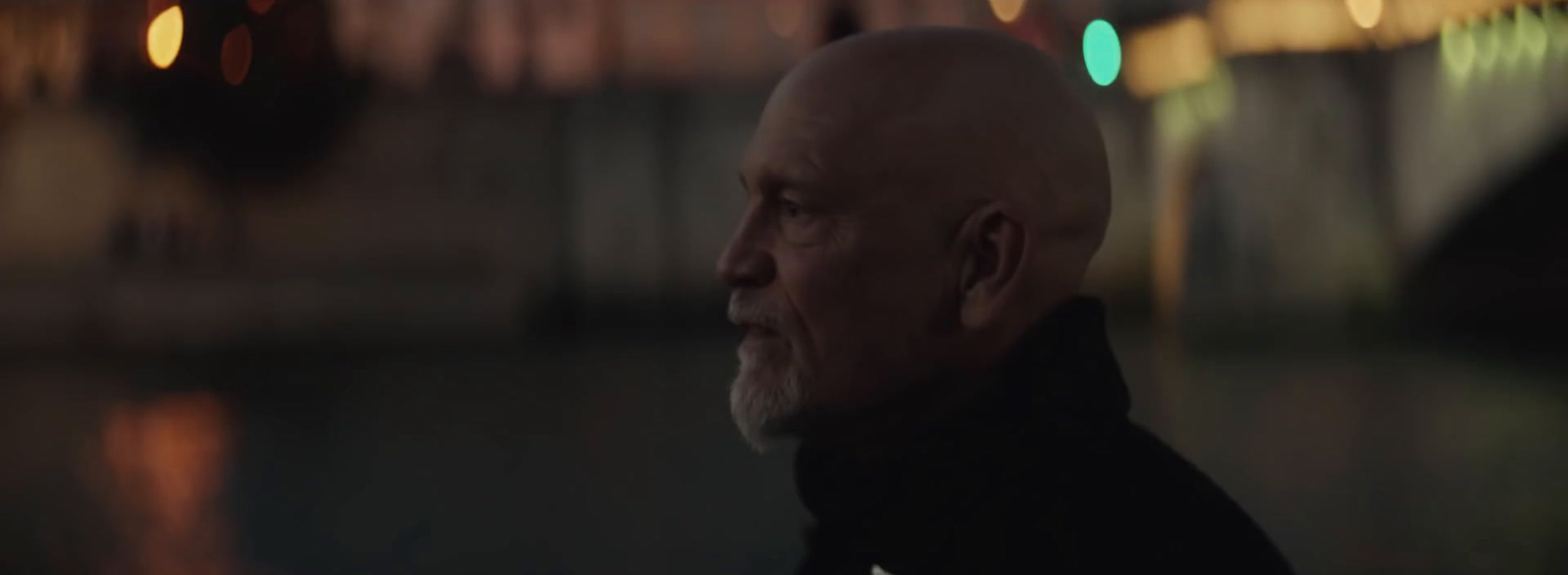 a bald man in a black jacket looking off into the distance