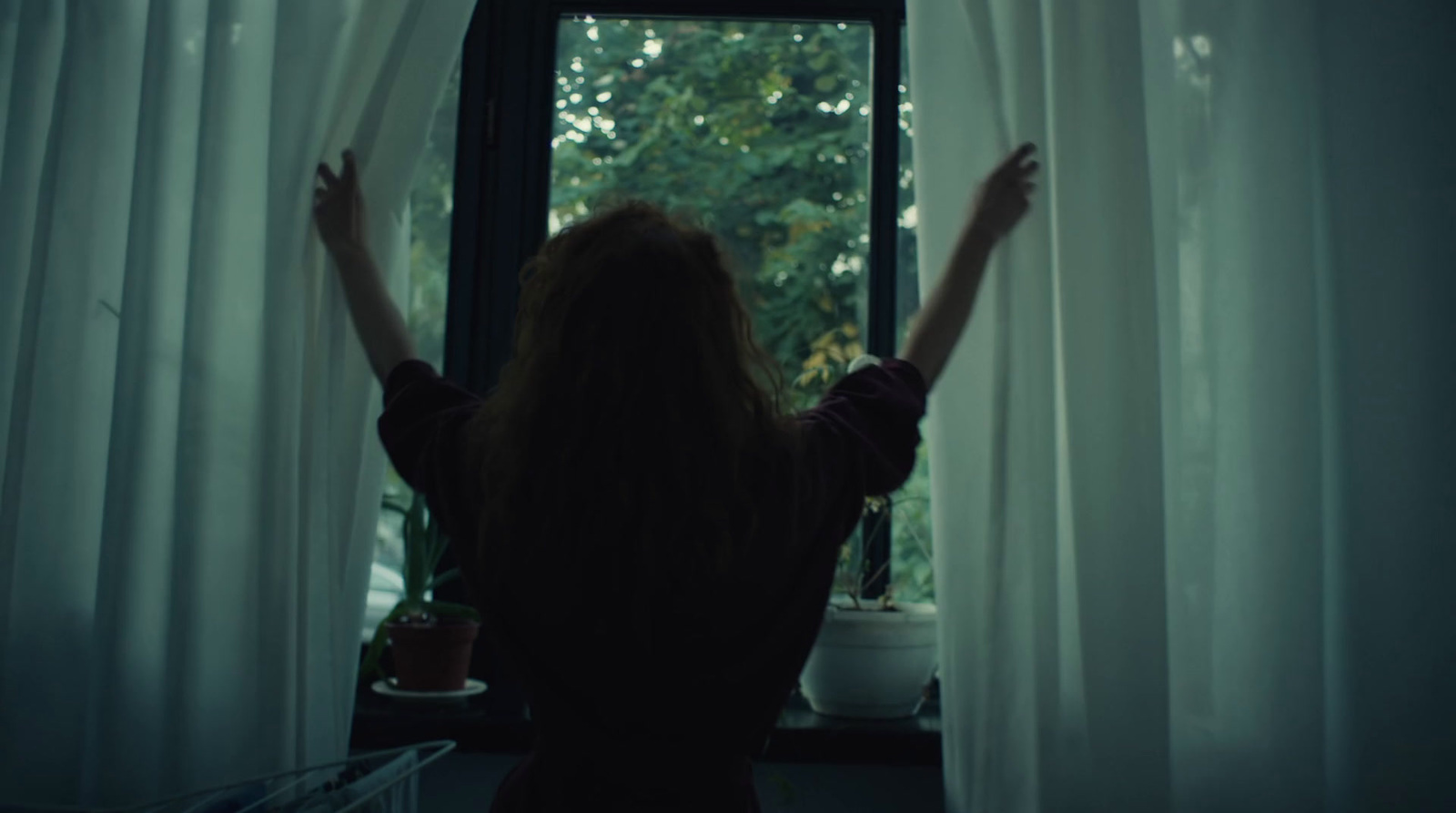 a woman standing in front of a window with her arms up