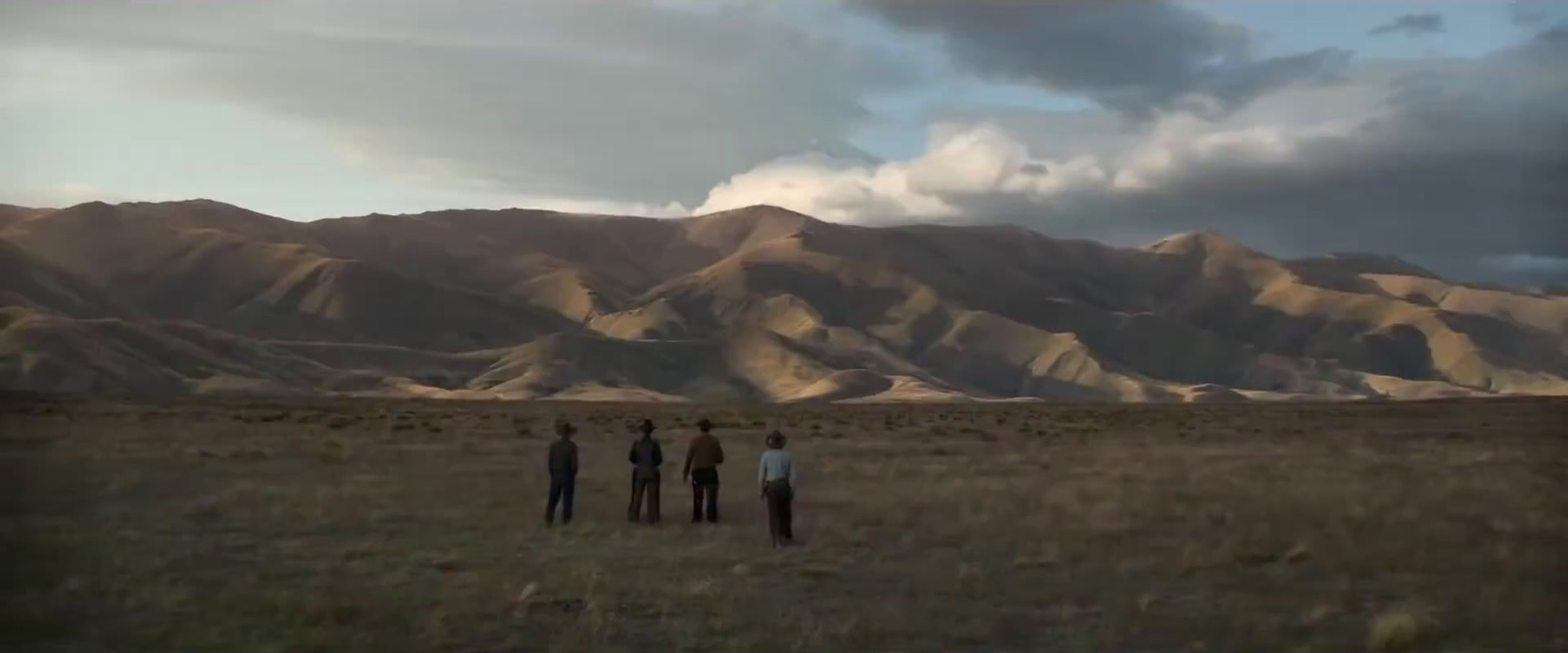 three people standing in a field with mountains in the background