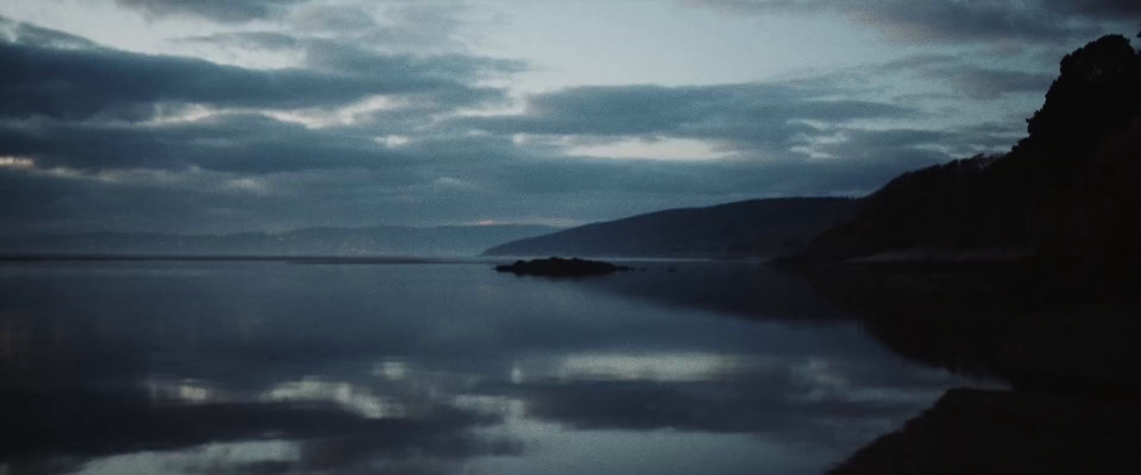 a body of water surrounded by mountains under a cloudy sky