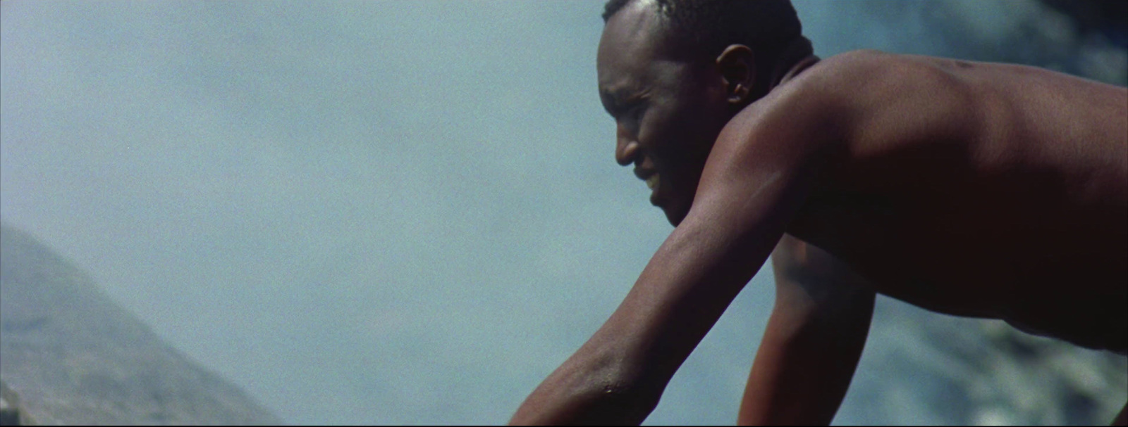 a man with no shirt standing in front of a mountain