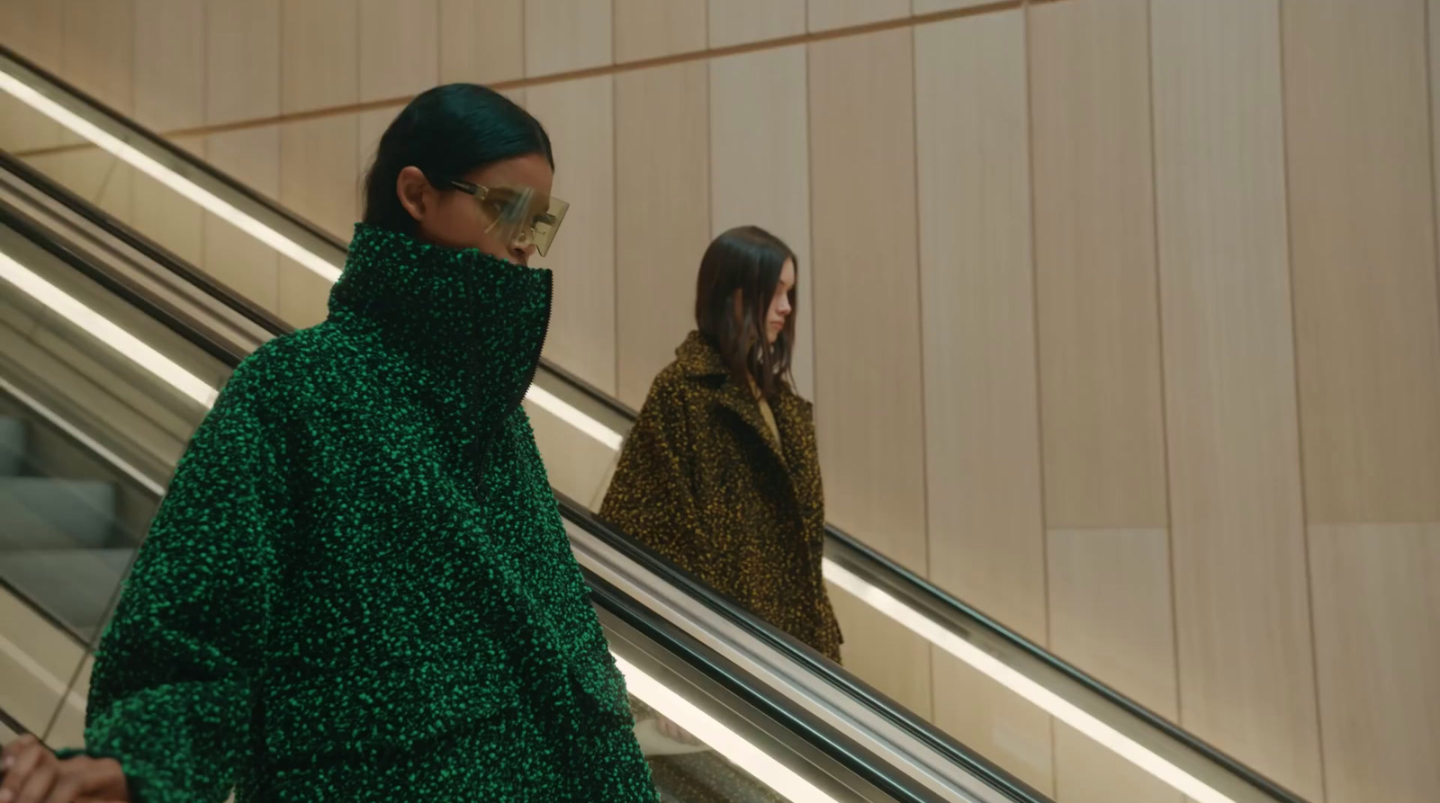 a woman in a green coat is riding an escalator