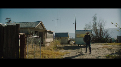 a man walking down a dirt road next to a shack