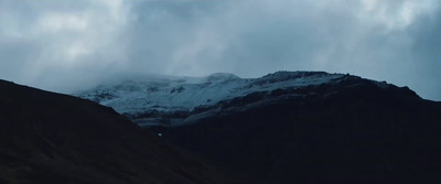 a mountain covered in snow under a cloudy sky