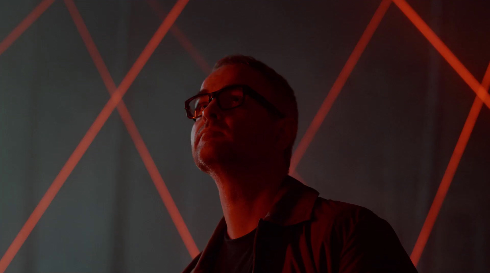 a man with glasses standing in front of a red light