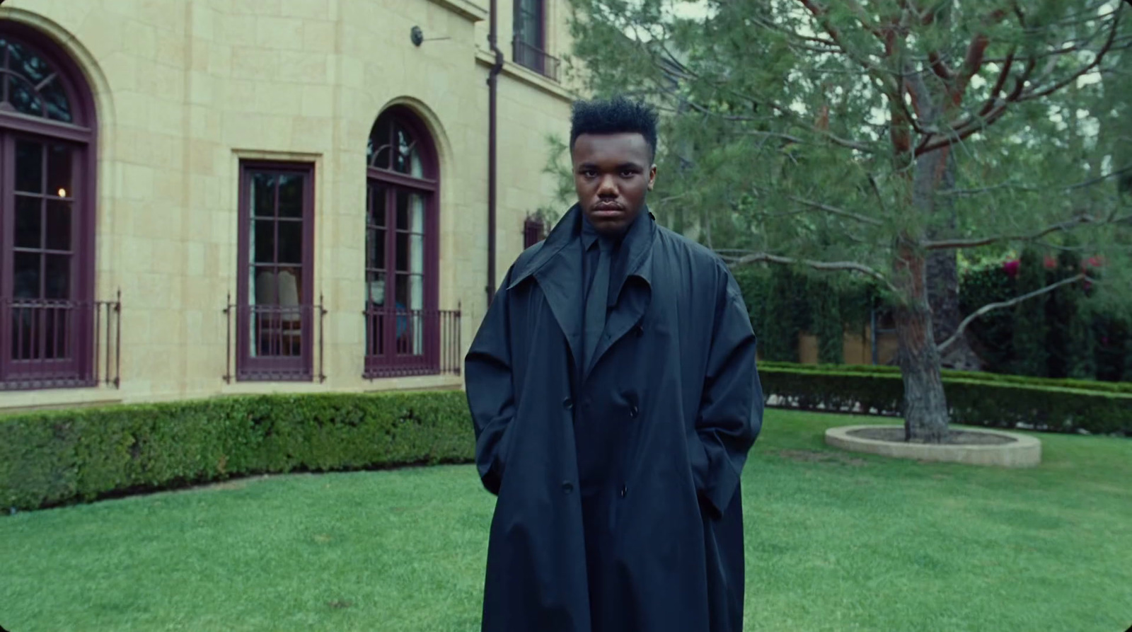 a man in a trench coat standing in front of a building