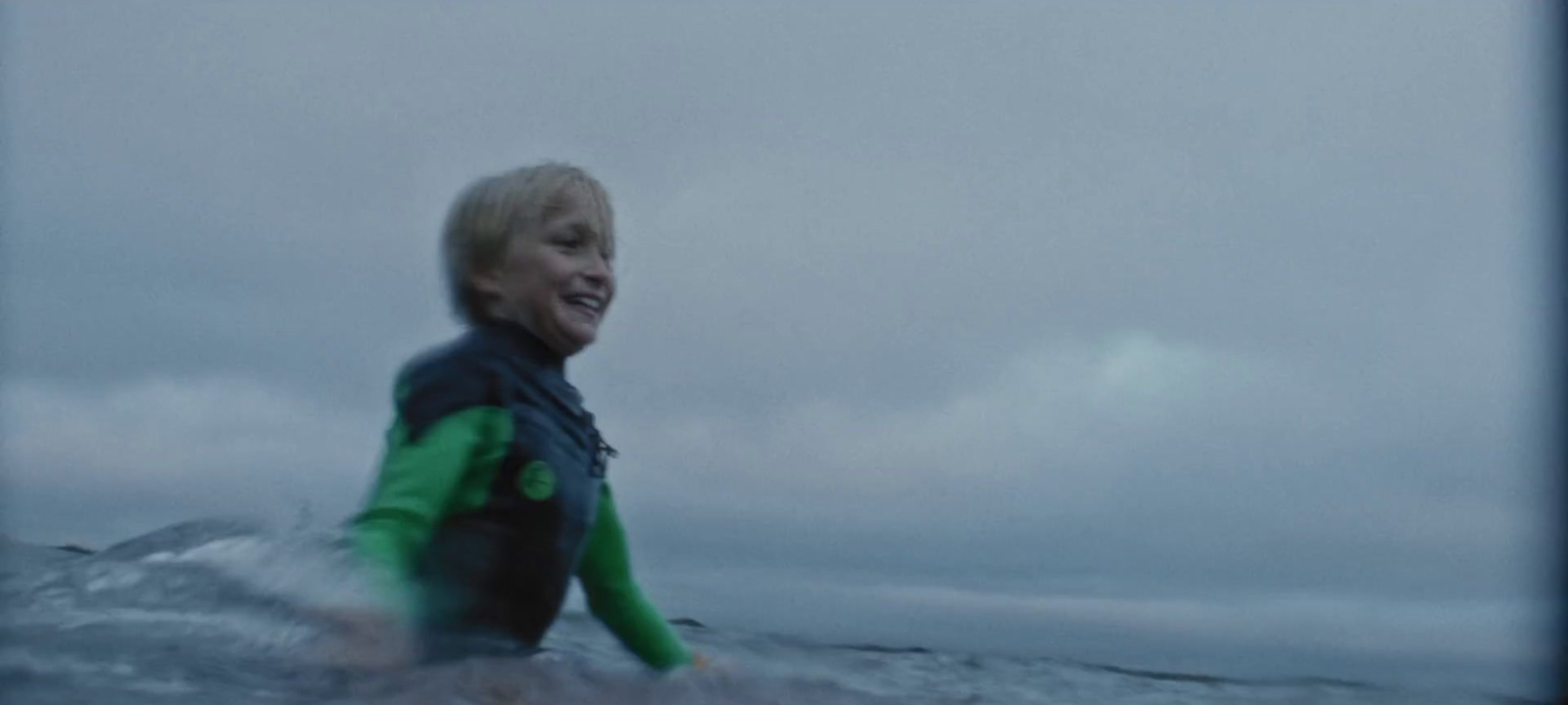 a young boy in a wet suit riding a surfboard