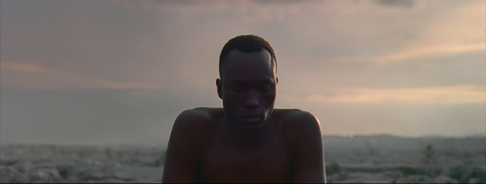 a man with no shirt standing in front of a cloudy sky