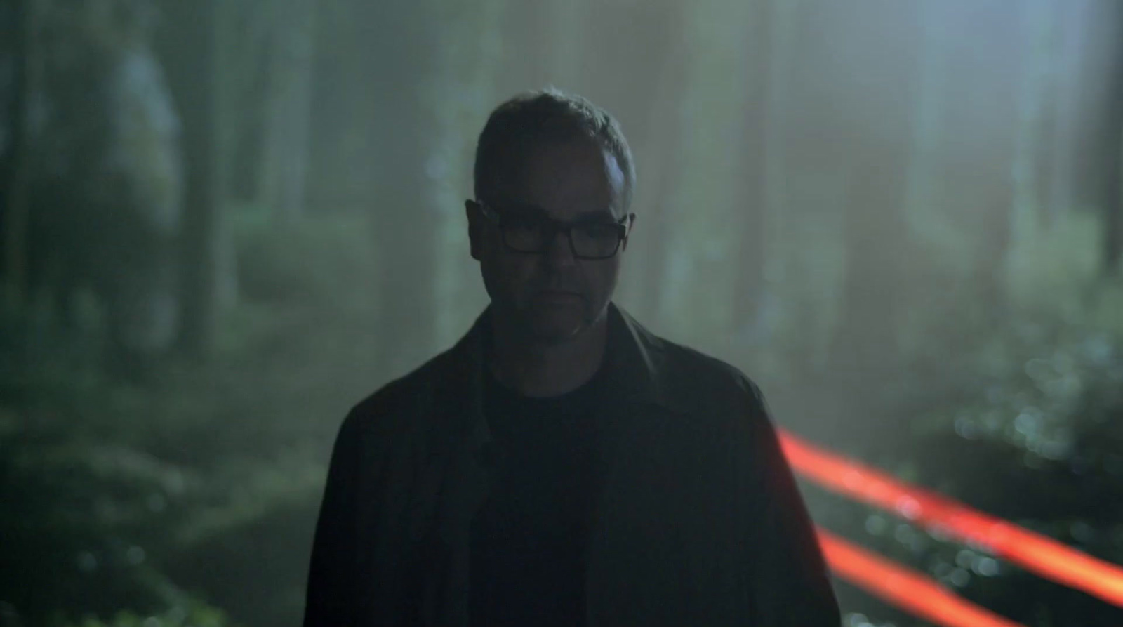 a man with glasses standing in a forest