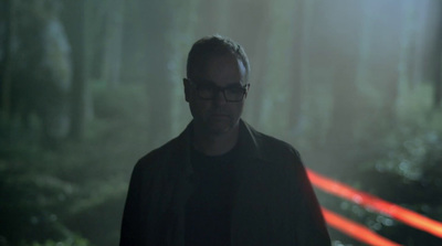 a man with glasses standing in a forest