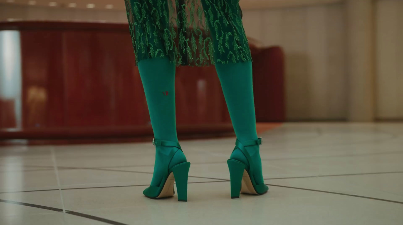 a woman in green high heels standing on a tile floor