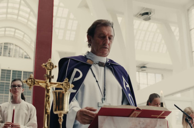 a priest standing in front of a cross in a church