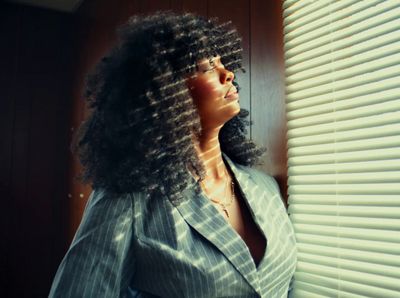 a woman standing next to a window covered in blinds