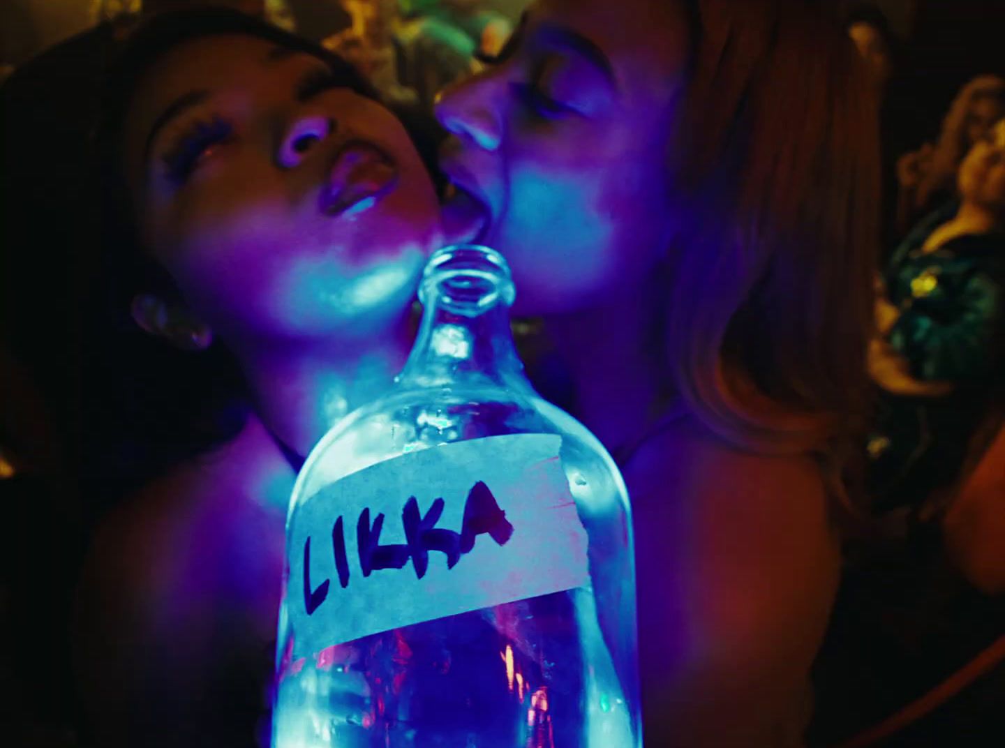 a couple of women sitting next to each other in front of a bottle